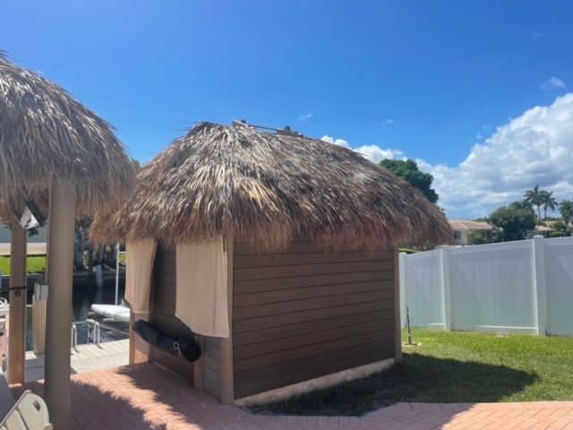 Thatched-roof cabana on a pool deck beside a white fence under a blue sky.