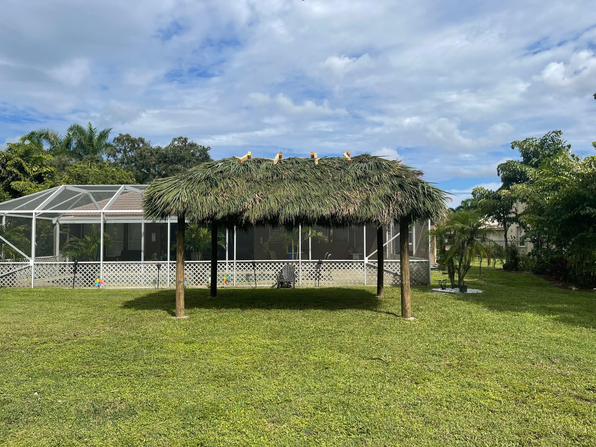 Grassy yard with a shaded gazebo in front of a white screened building under a cloudy sky