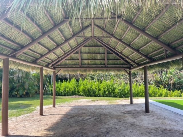 Thatched-roof pavilion with wooden posts in a grassy garden area
