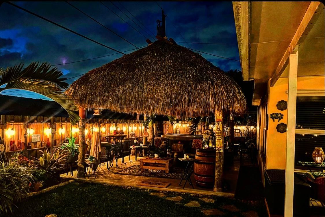 Tropical thatched-roof restaurant lit warmly at dusk with outdoor seating and palm trees