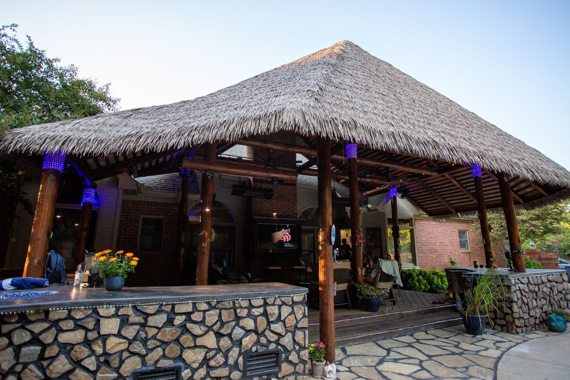 Tropical thatched-roof patio with stone walls and wooden posts outside a restaurant