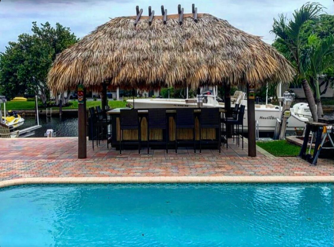Tropical poolside bar with a thatched roof beside a turquoise swimming pool