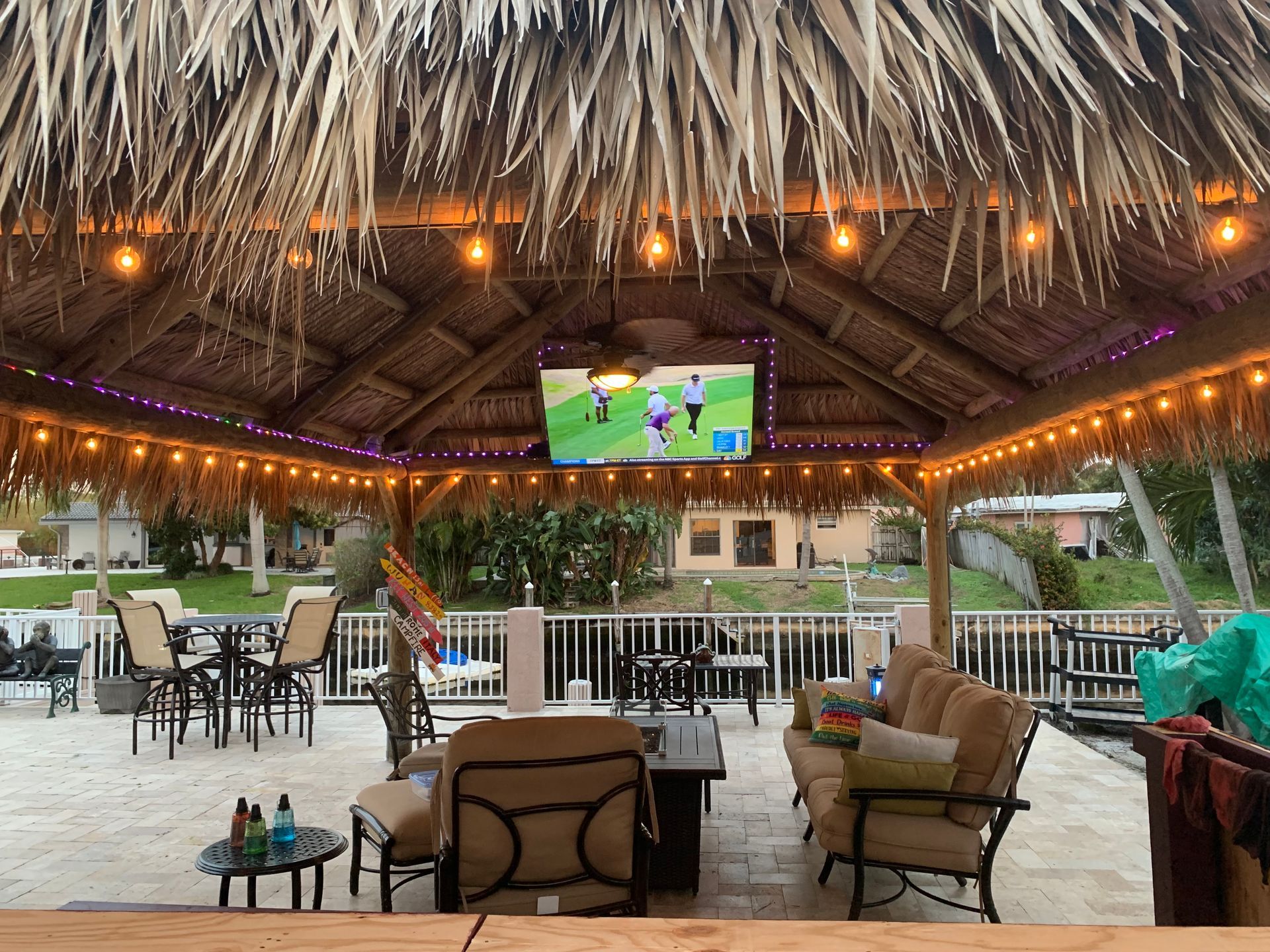 Thatched beach bar with outdoor seating and a TV showing a soccer match