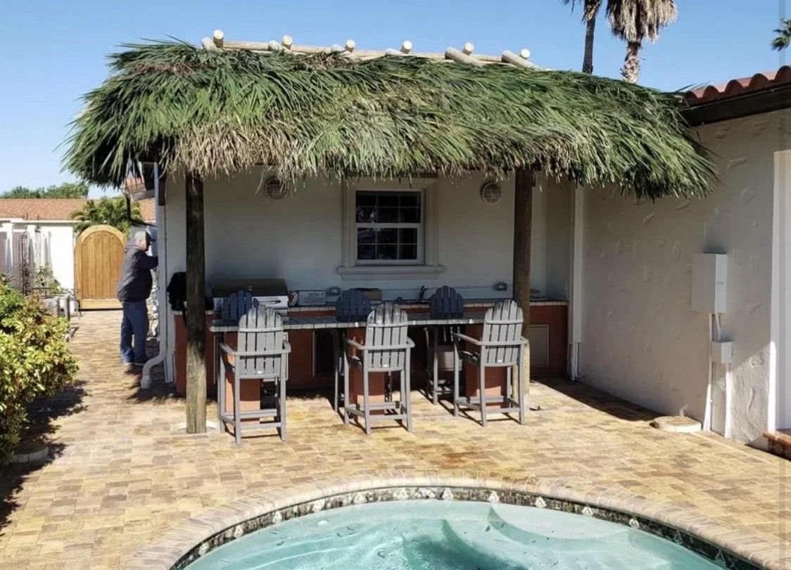 Patio with table and chairs under a thatched roof beside a small pool