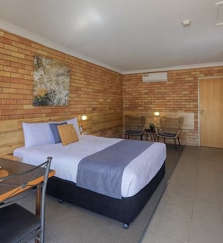 Bedroom with brick walls, black bed, wooden wardrobe, small table and chairs.
