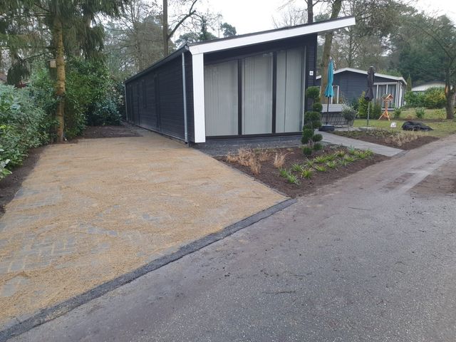 Moderne zwart-witte blokhut naast een grindpad in een bosrijke woonwijk.