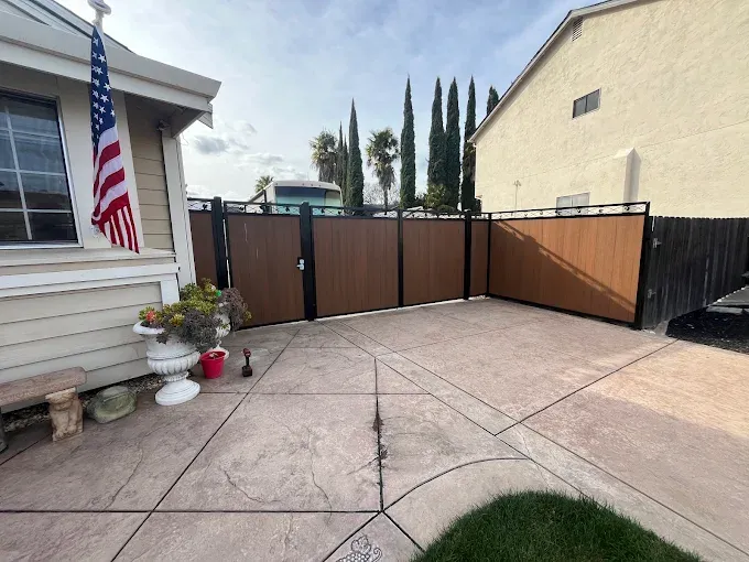 Backyard patio with brown and black fence, American flag, and potted flowers.