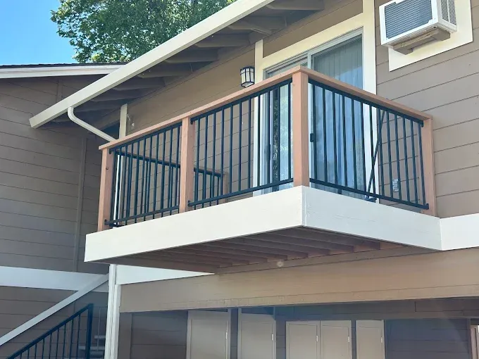 Balcony with black railing and brown wooden trim; beige building exterior.