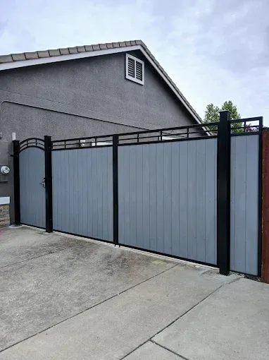 Gray wooden privacy gate with black metal frame in front of a house.
