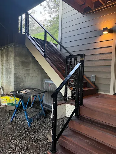 Exterior staircase with black metal railing and cable infill, connecting a wooden deck to the ground.