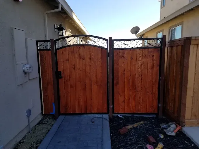 Wooden double gate with arched tops, framed in black metal, in a backyard setting.