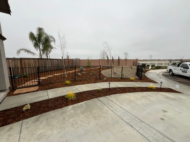 Curved sidewalk and landscaped median beside a parking lot under cloudy skies, with palm trees and parked cars.