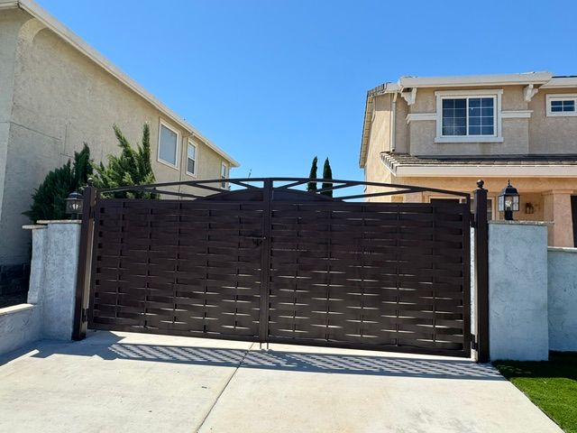 Dark brown driveway gate between two tan houses under a clear blue sky