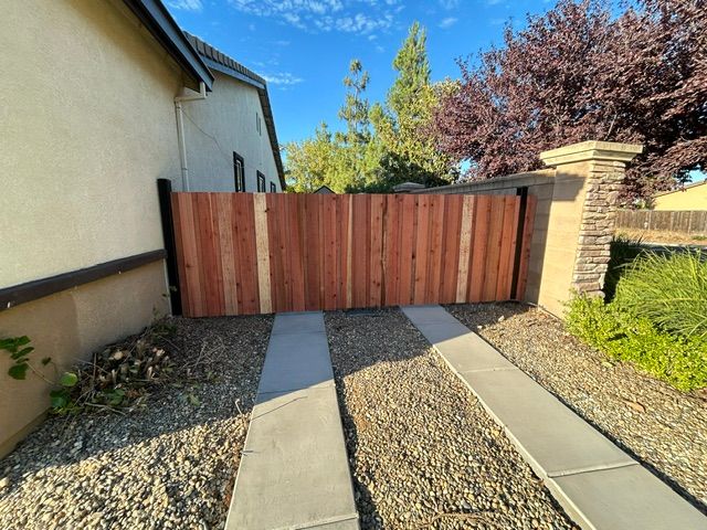 Driveway leading to a closed wooden gate beside a stucco house and brick pillar