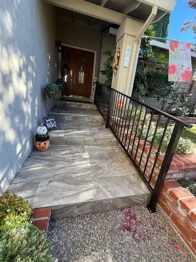 Exterior view of a home's entrance, with steps leading to a wooden door. A black railing is along the steps.