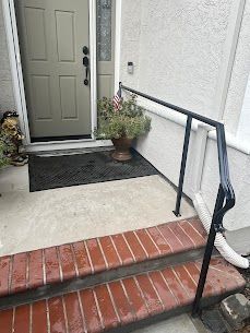Exterior view of a home entrance with a black handrail for accessibility, leading to a front door with steps.
