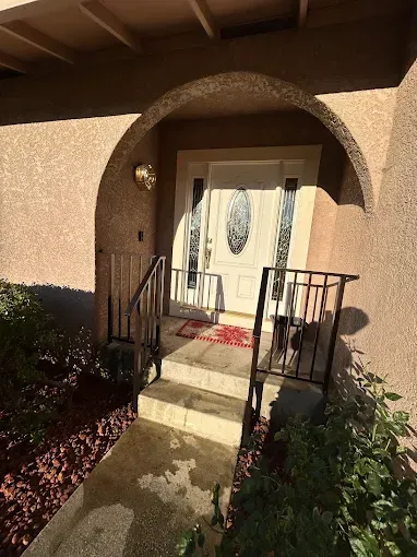 Front entrance of a house with an arched entry. Steps lead to a white door. Black railing.