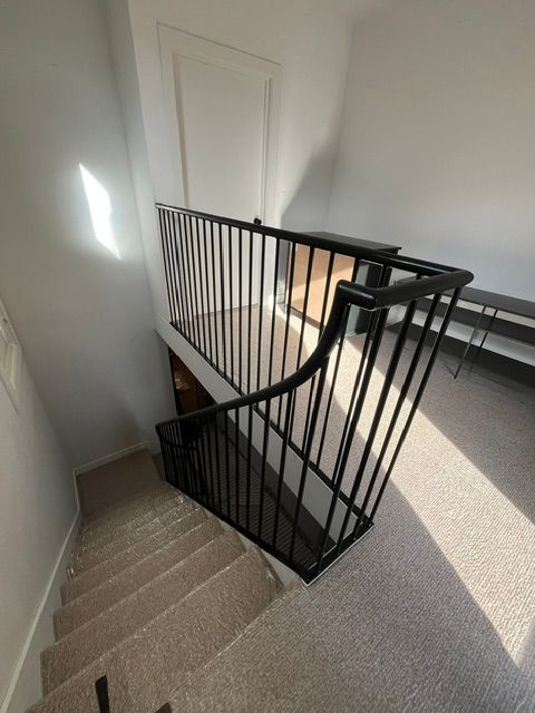 Stairwell with carpeted steps, black metal railing, and white walls beside a landing.