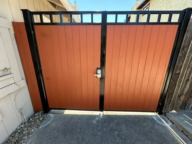 Orange wooden double gate with black frame and latch at the end of a driveway