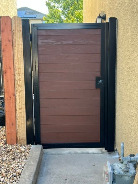 Closed brown wooden gate in a black frame beside a concrete path and gravel yard
