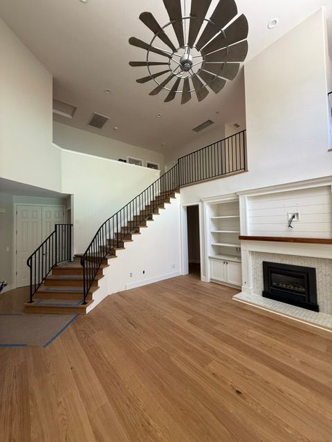 Empty living room with hardwood floors, staircase, modern ceiling fan, and fireplace mantel