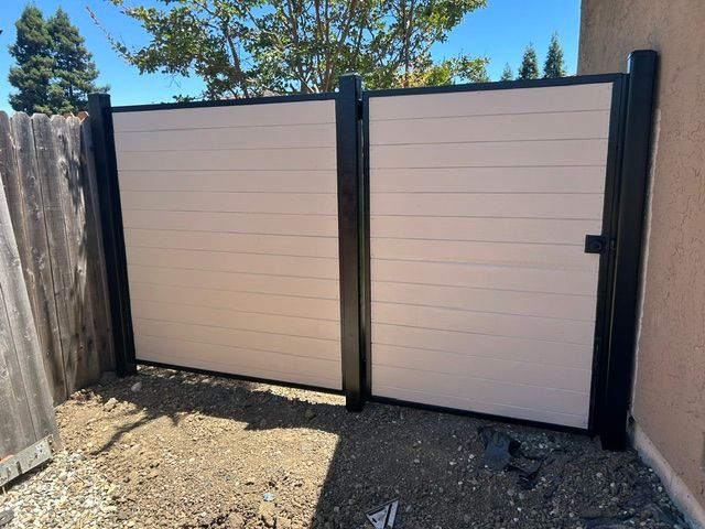 Two cream privacy gates in a narrow outdoor side yard with gravel and wood fencing.