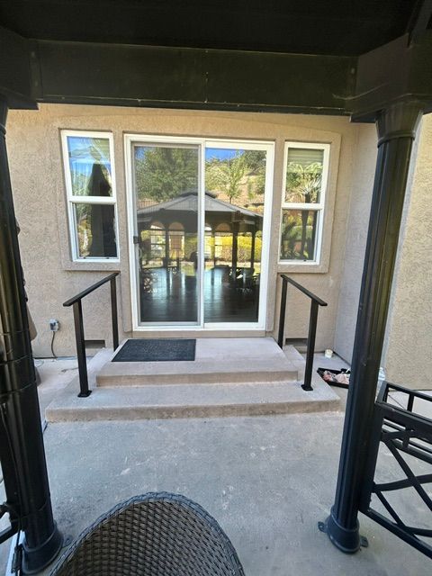 Front porch steps leading to sliding glass doors, with black railings and windows on either side
