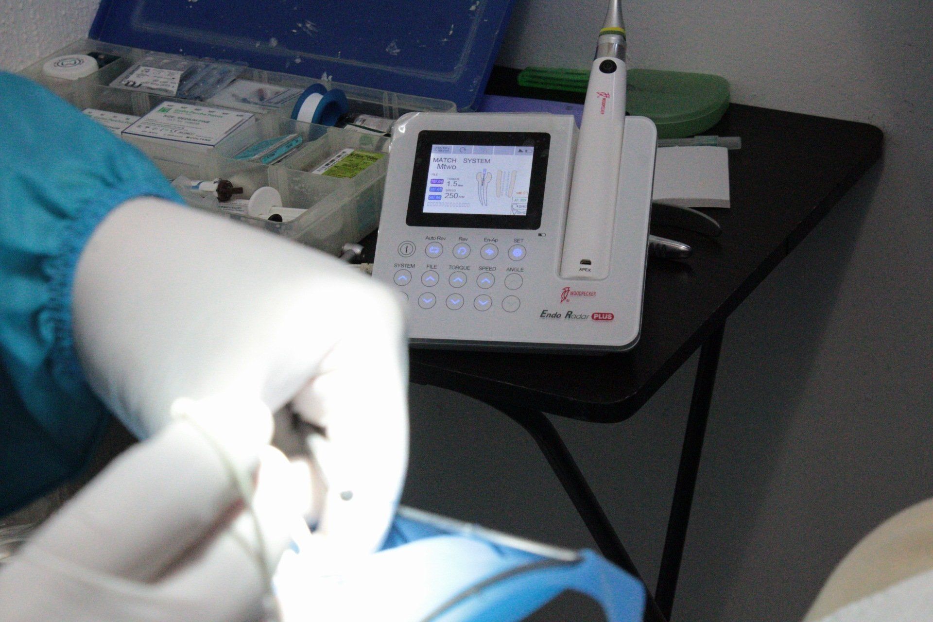 En una clínica, unas manos enguantadas trabajan en un modelo dental junto a un monitor y un panel de control.