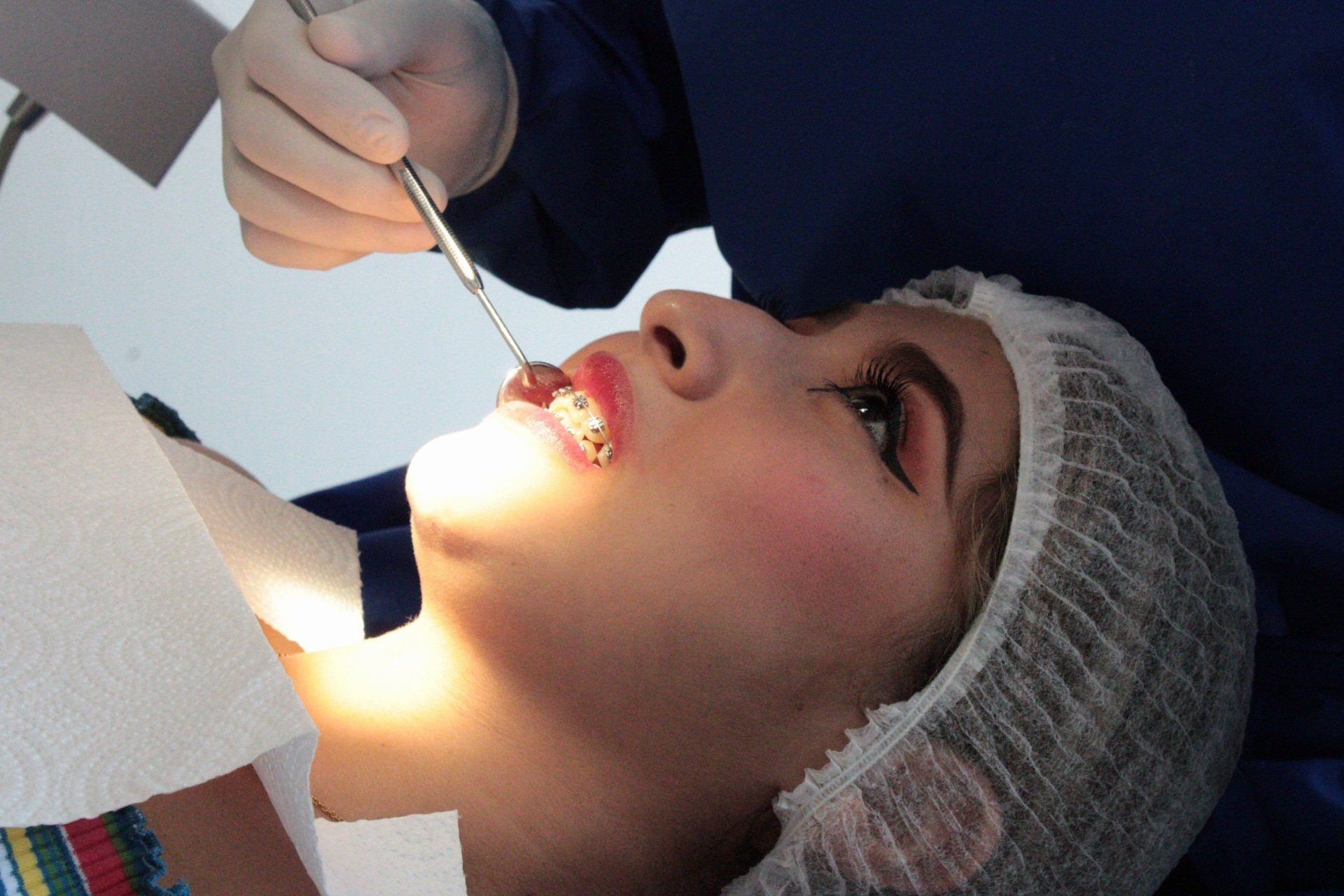 Odontólogo examinando la boca de un paciente con un instrumento dental bajo luz brillante.