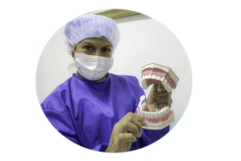 Profesional dental con uniforme morado mostrando una dentadura postiza mientras usa mascarilla y gorro.