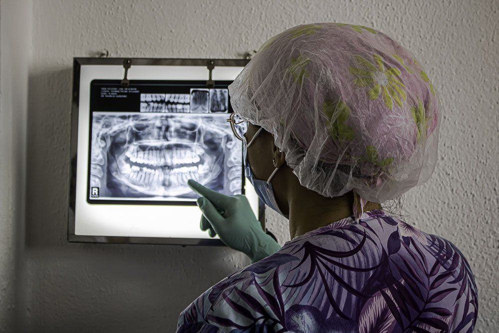 Un dentista con bata morada señala una radiografía dental panorámica en una caja de luz.