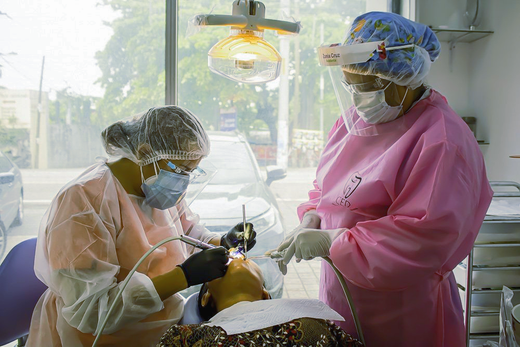 Dentistas con mascarillas y protectores faciales atendiendo a un paciente en una luminosa clínica dental.