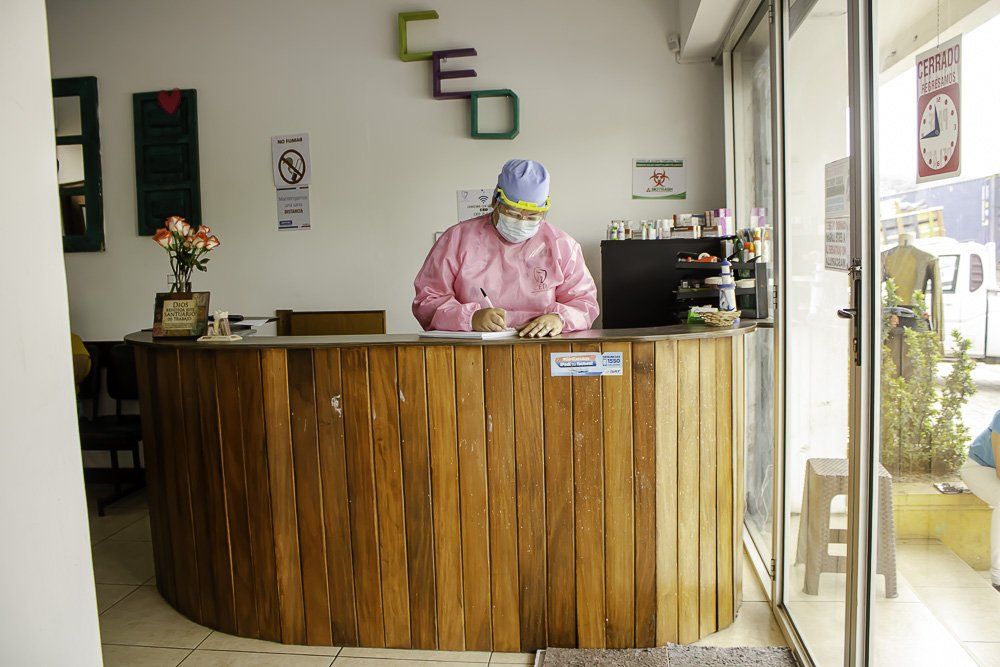 Persona con ropa protectora rosa trabajando detrás de un mostrador de recepción de madera en el interior.