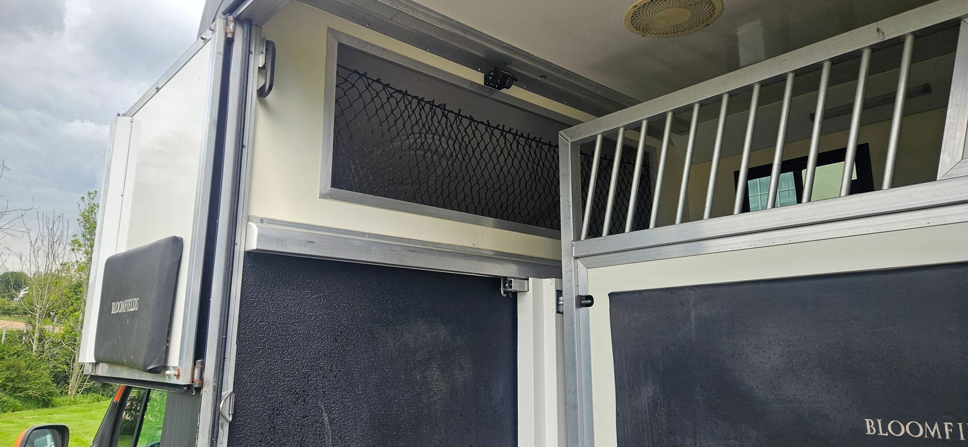 White vehicle side with black vent panels and a small balcony railing above on a sunny day