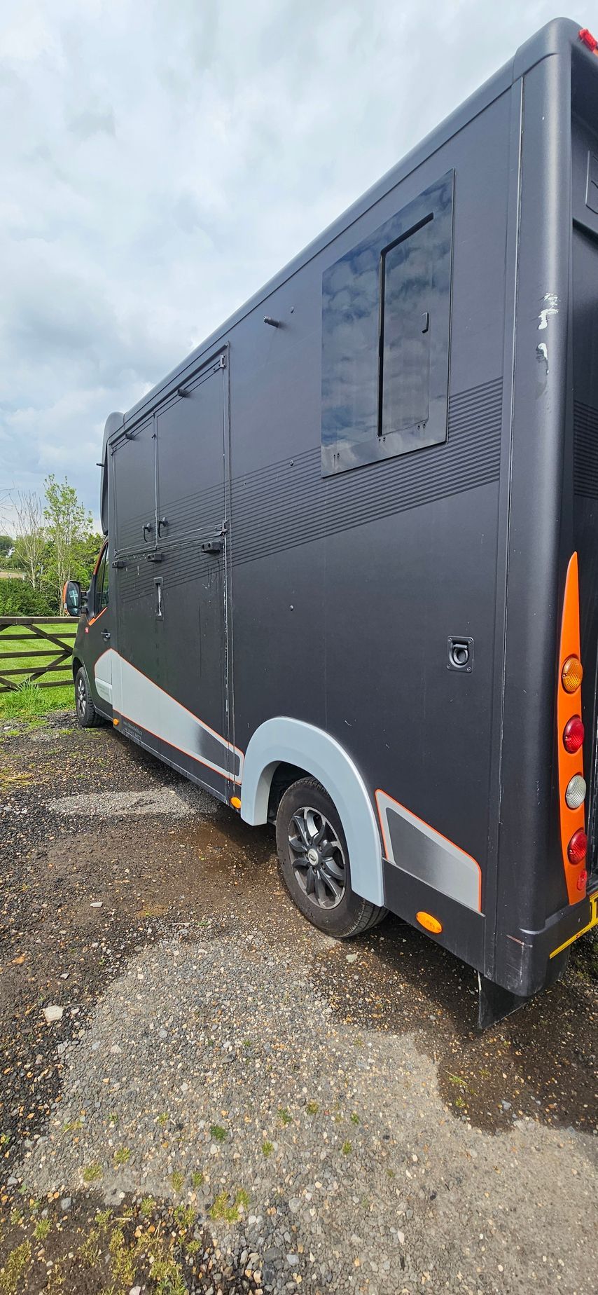 Dark gray enclosed trailer parked on gravel, side view with orange reflectors and white wheel fender.