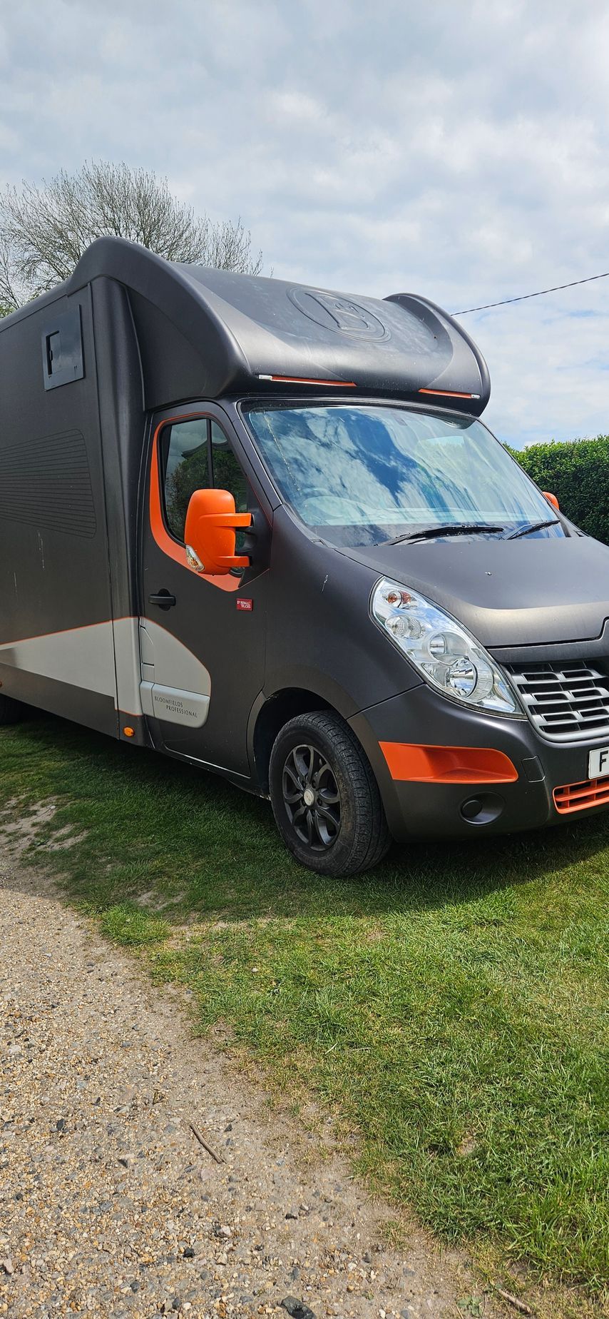 Black and gray camper van parked on grass, with orange accents and a cloudy sky overhead