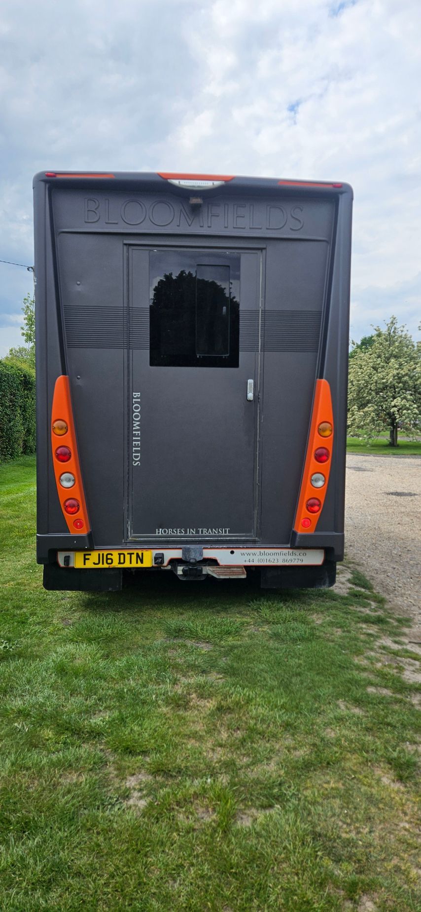 Rear view of a dark gray cargo van with red tail lights, parked on grass with an open rear window panel.