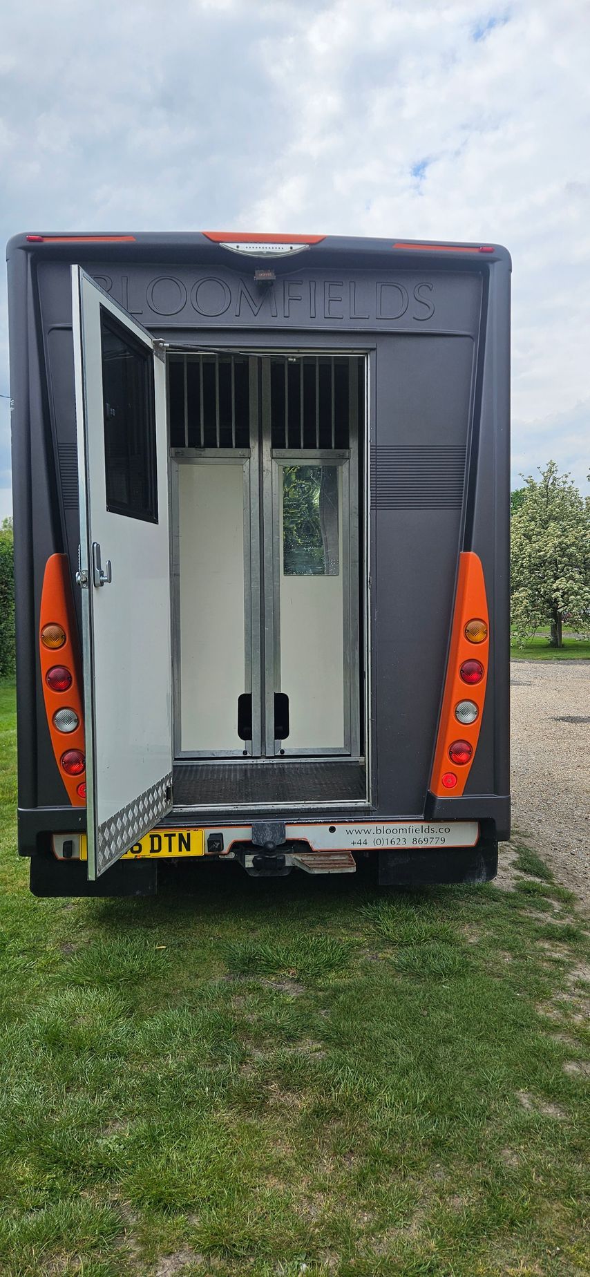 Rear view of a gray box truck with open cargo door, parked on grass.