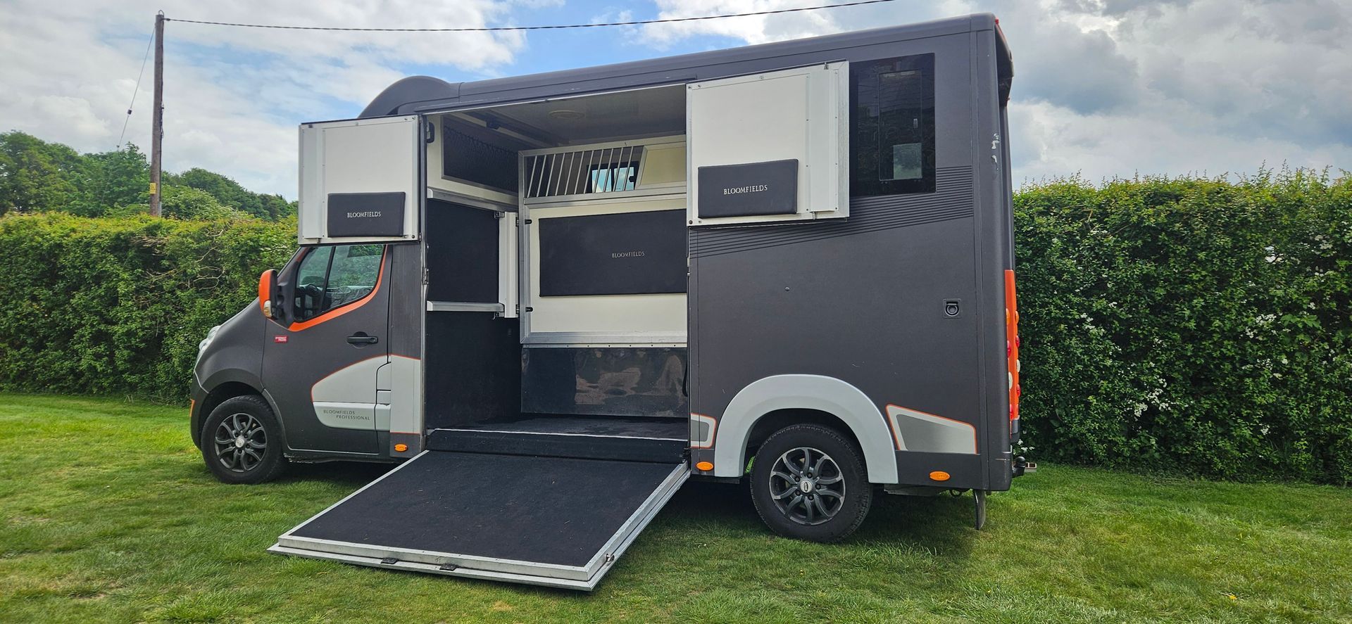 Black box-style camper truck with an open side hatch and ramp on a grassy lawn