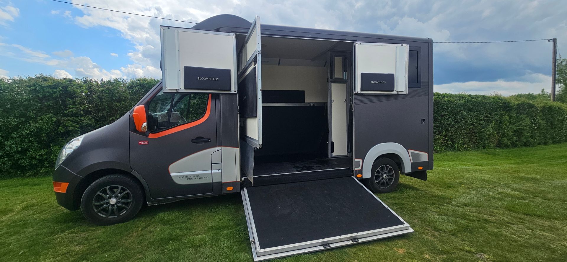 Accessible van with side ramp and open compartments parked on grass