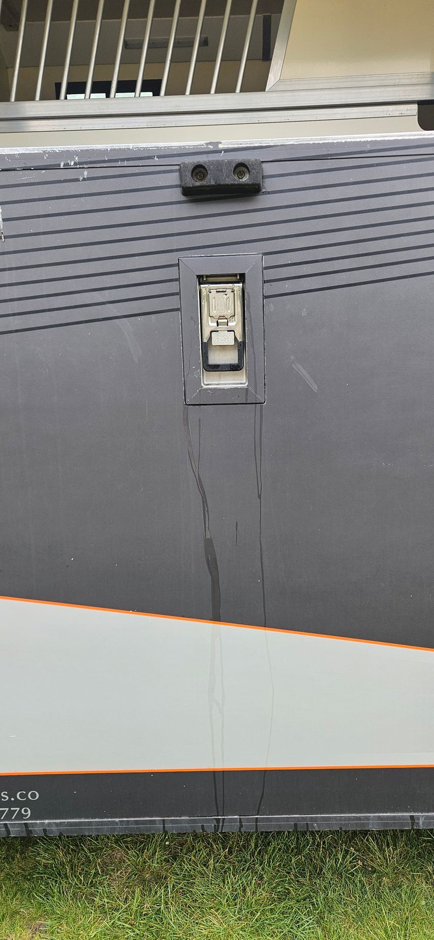 Gray utility cabinet with vented top, small latch, and grass at the bottom edge
