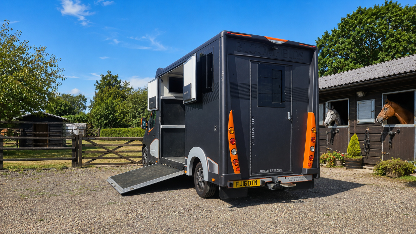 Black horse trailer with ramp parked on a gravel driveway beside a house on a sunny day