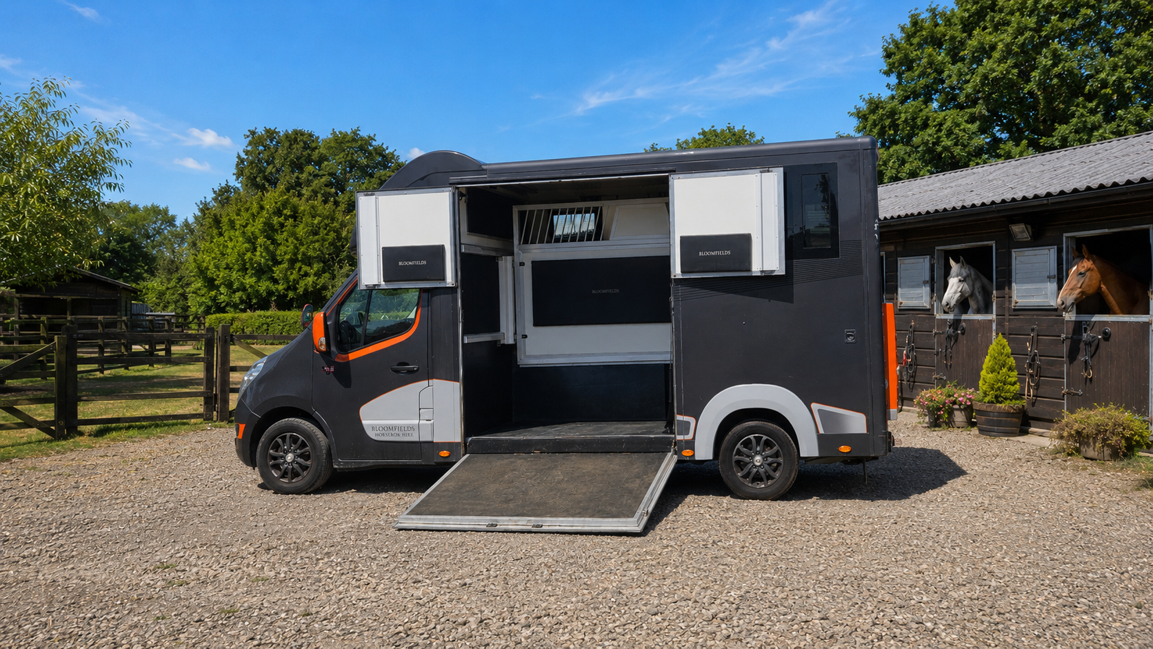 Black and white food truck with open serving hatch parked on gravel by a building and fence under blue sky