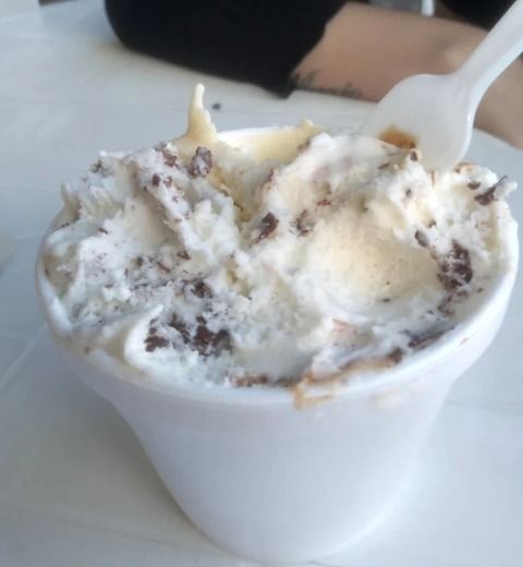 Una taza blanca de helado de galletas y crema con una cuchara sobre una mesa.