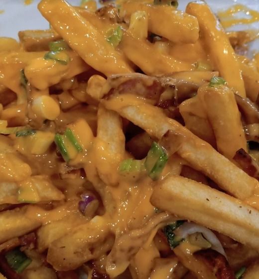 Primer plano de papas fritas con salsa, cubiertas con salsa cremosa de naranja y cebolla verde picada.
