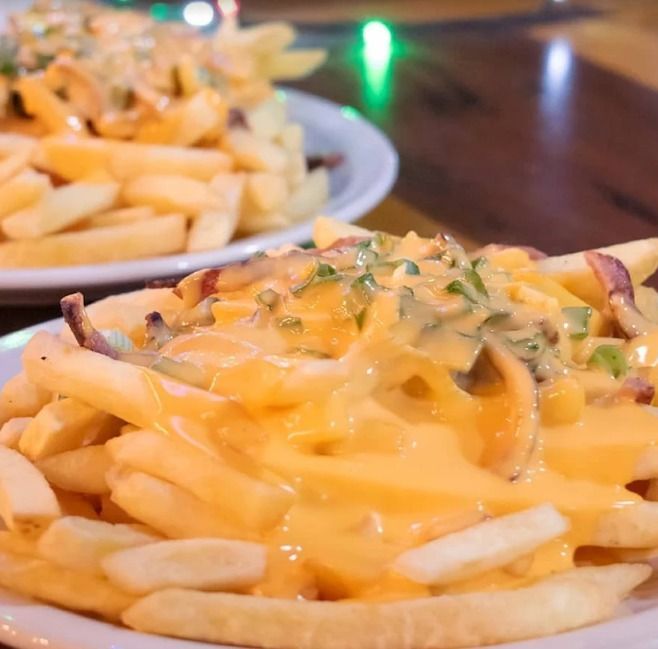 Papas fritas con queso en una cesta con salsa y hierbas, con otro plato de papas fritas al fondo.