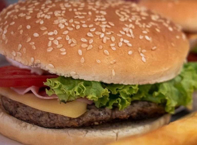 Primer plano de una hamburguesa con semillas de sésamo, lechuga, tomate, queso y carne de res en un panecillo.