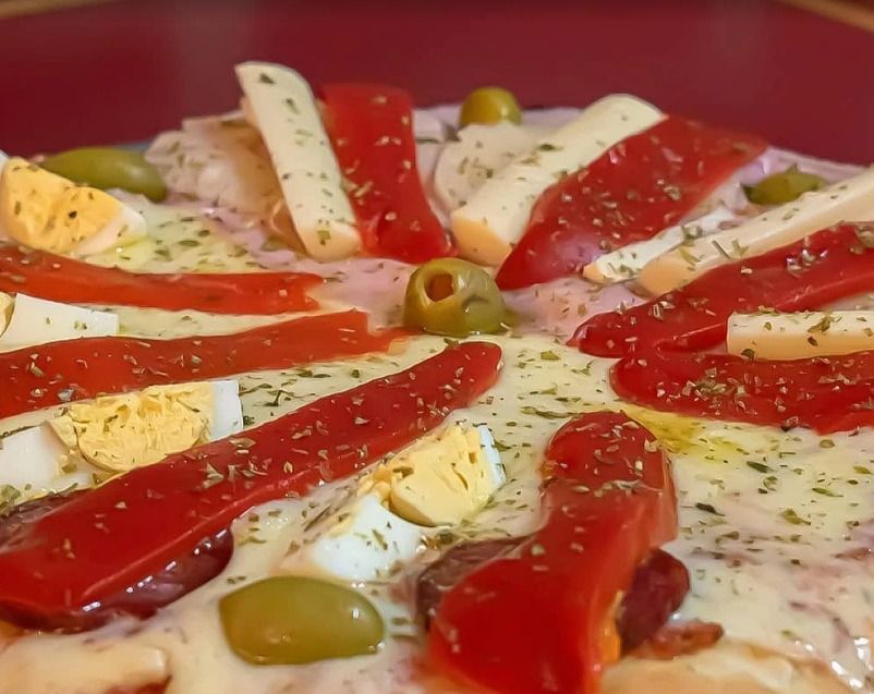 Primer plano de una pizza cubierta con pimientos rojos, aceitunas y queso fundido.