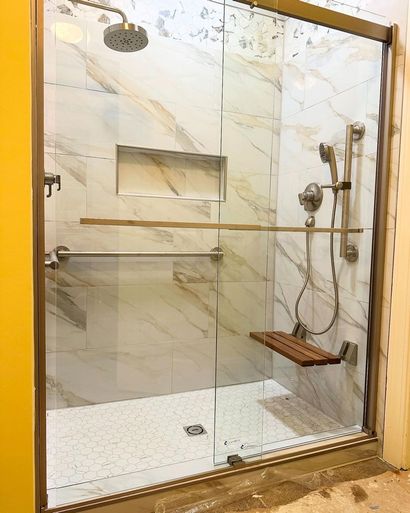 Modern glass shower with marble tile, gold trim, built-in niche, and handheld showerhead