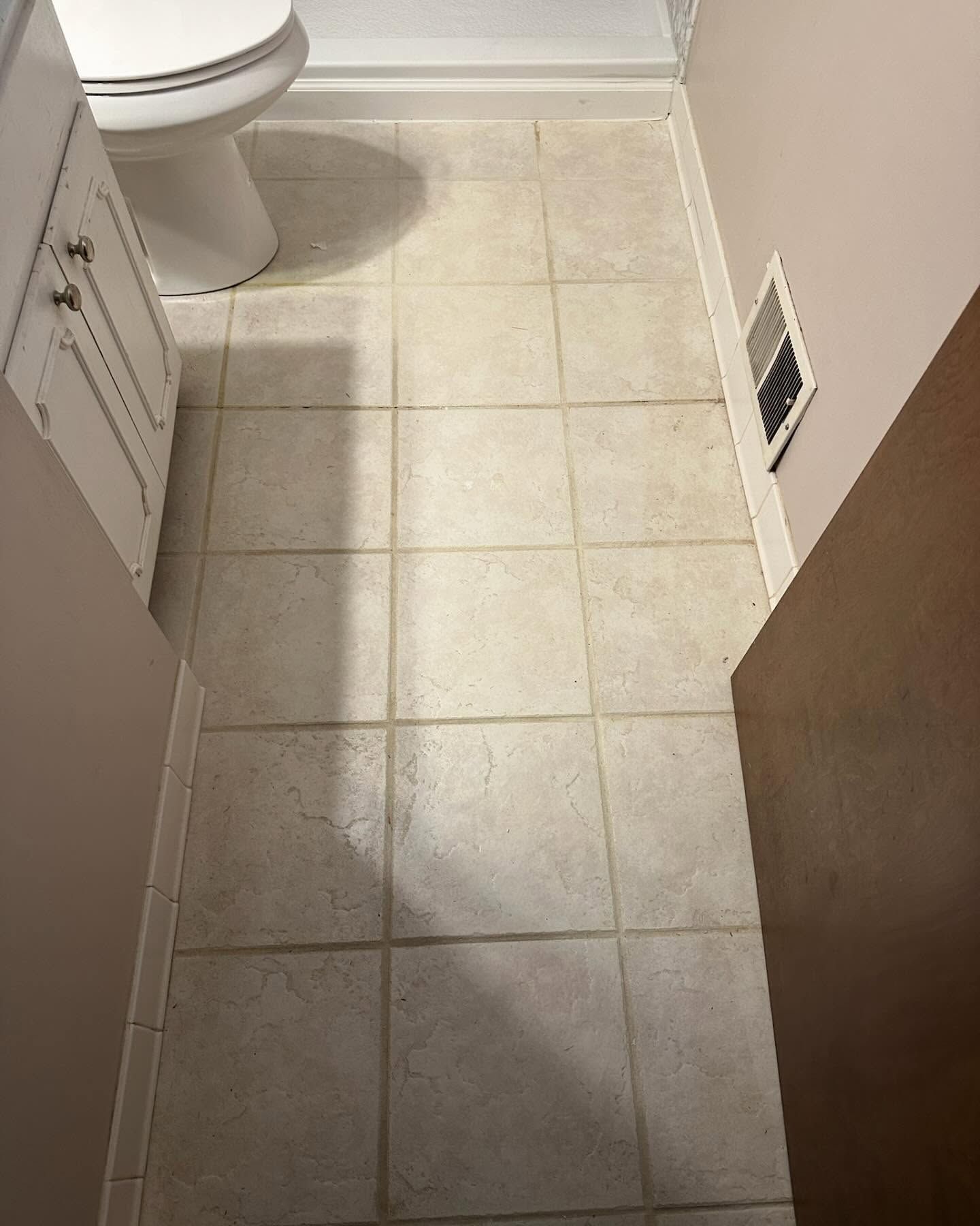 Small tiled bathroom floor with toilet, vanity edge, and wall vent
